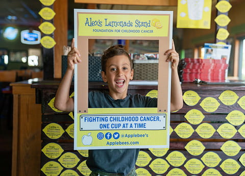 Child holding Alex's Lemonade Stand sign fundraising for childhood cancer